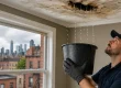 A professional roof repair technician catching water from a leaking ceiling in a bucket to prevent interior water damage.