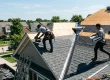professional roofers actively installing a new asphalt shingle roof on a suburban home, showing the full removal, underlayment, and Roof Installation work on a sunny day.